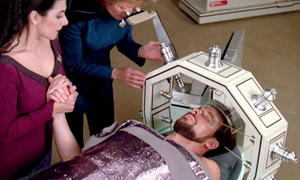 Szenenbild aus "Shades of Gray": Troi und Dr. Pulaski stehen neben Riker auf der Krankenstation