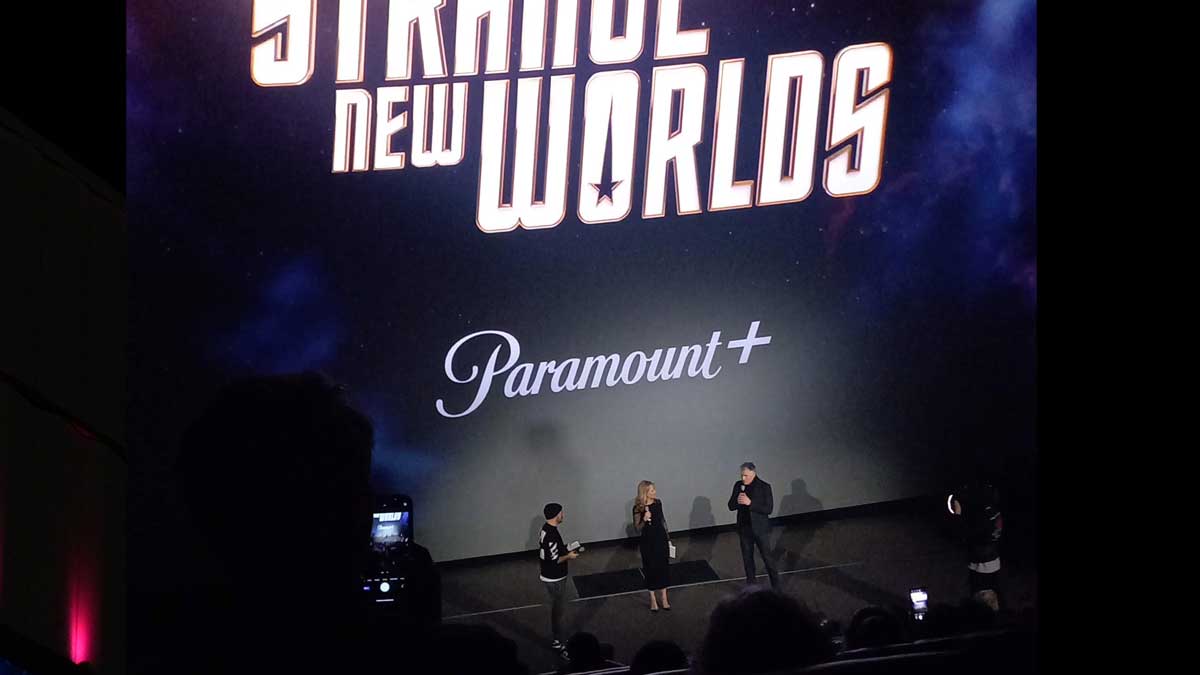 Paramount+ Launch Party. Dunkler Kinosaal, Logo von Star Trek auf der Leinwand, Anson Mount mit Mikrofon im Spotlight